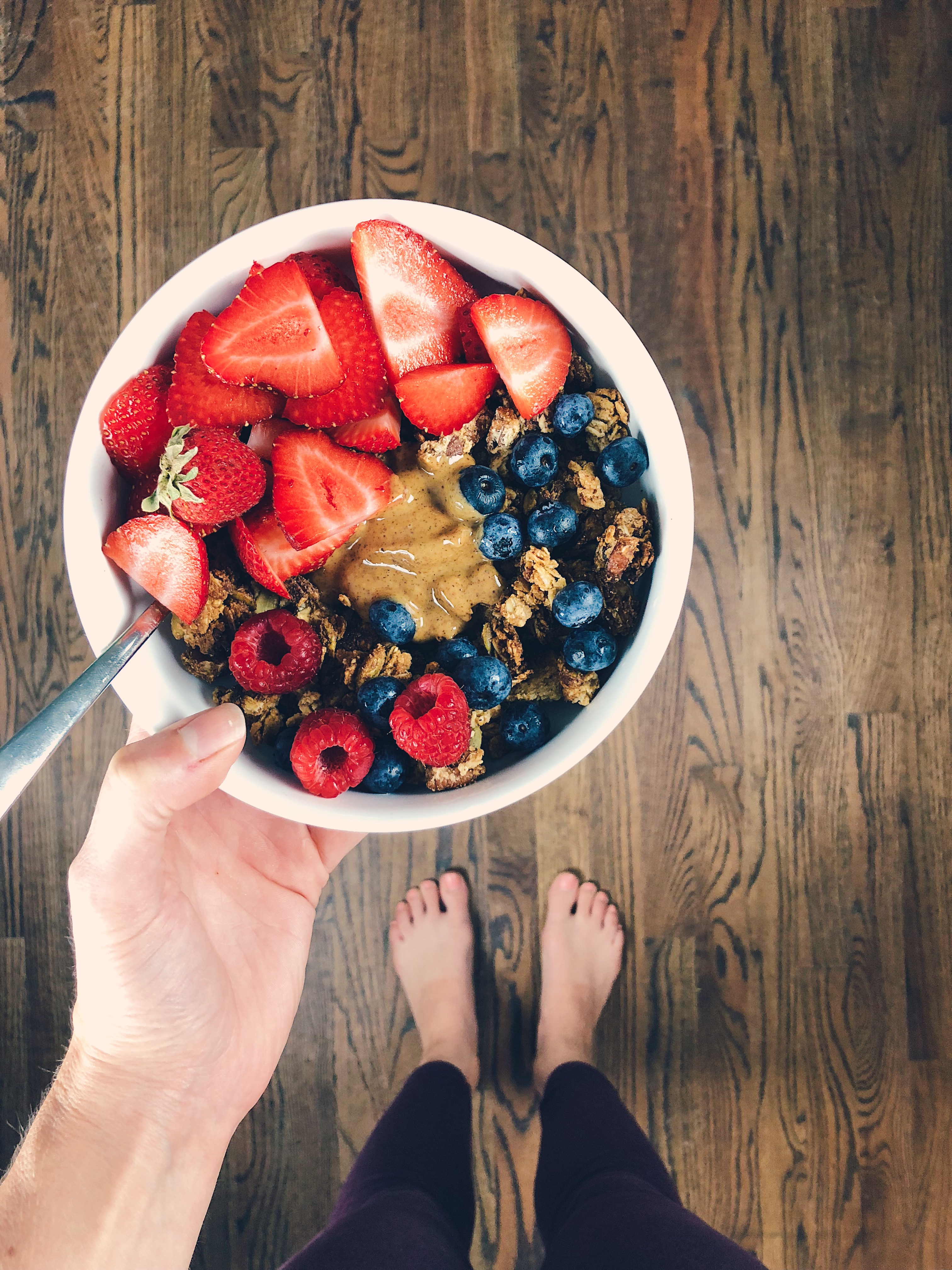 vegan and gluten free granola bowl with berries and peanut butter in white bowl being held