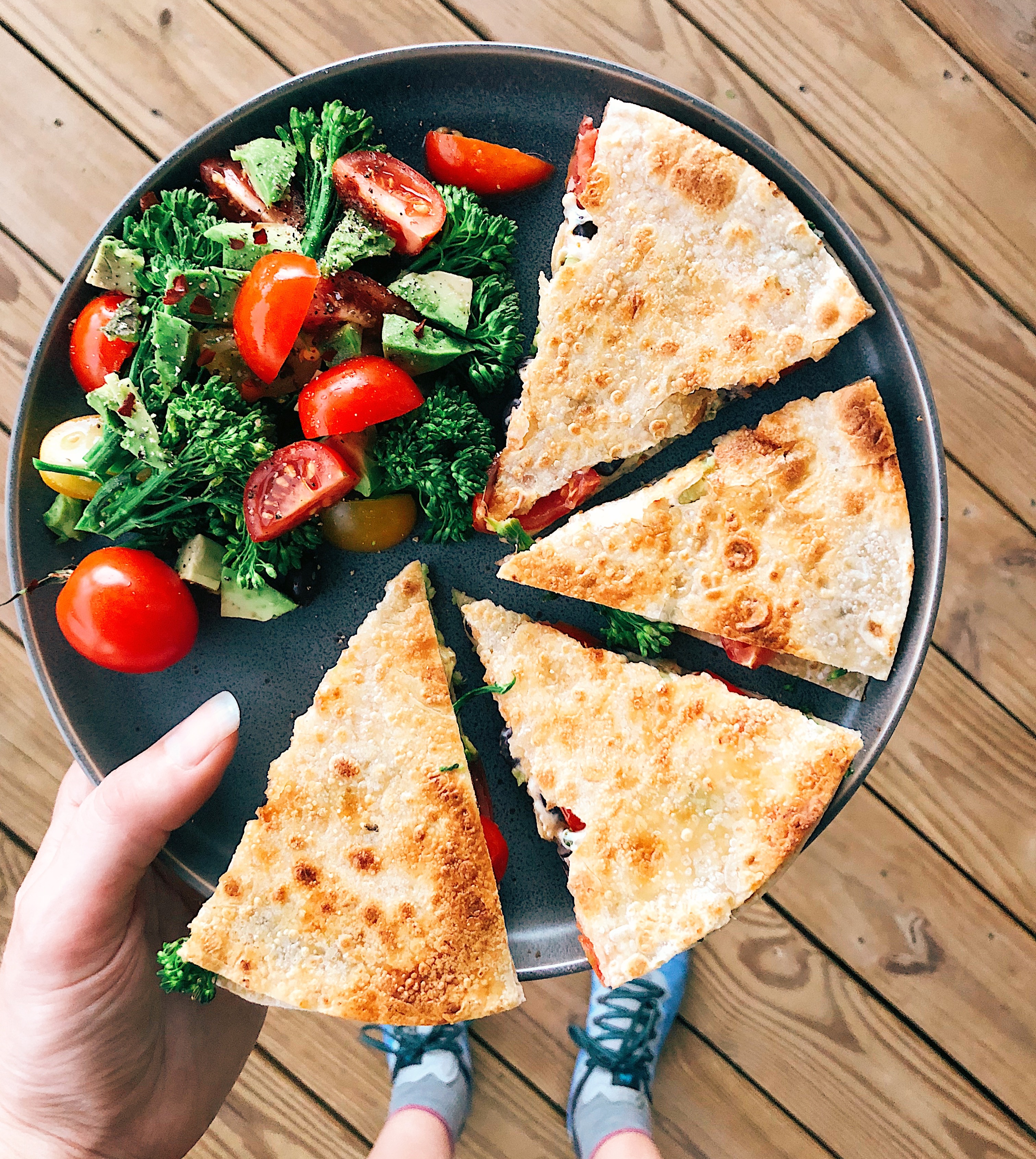 vegan quesadillas with broccolini salad on blue plate being held in the air