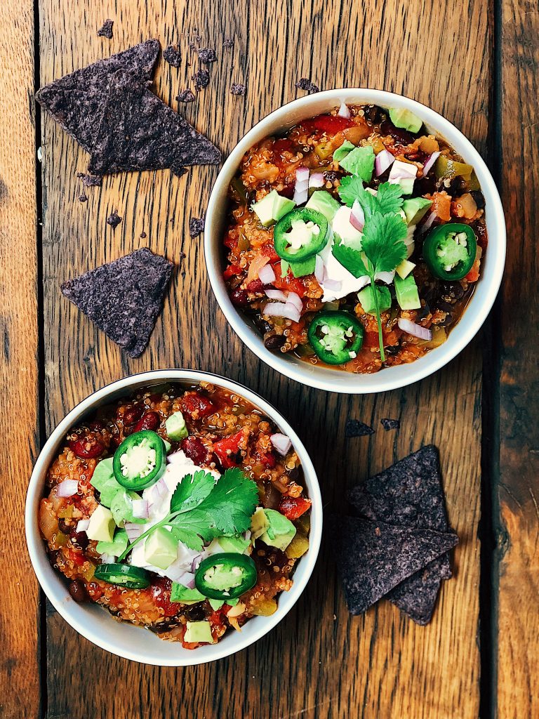 vegan chili in bowls with corn tortilla chips sour cream avocado jalapeno and cilantro on wood table
