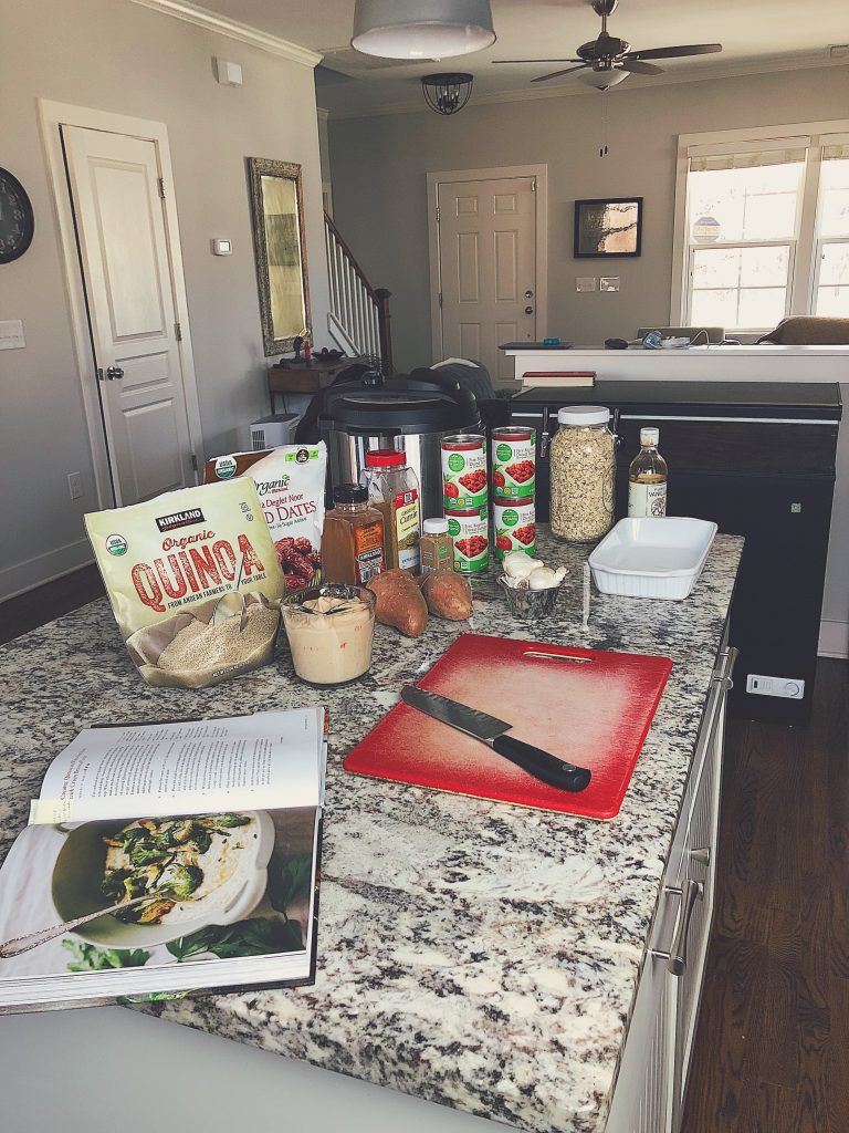 meal prep set up with cookbook, quinoa, cutting board, knife, and cans of tomatoes